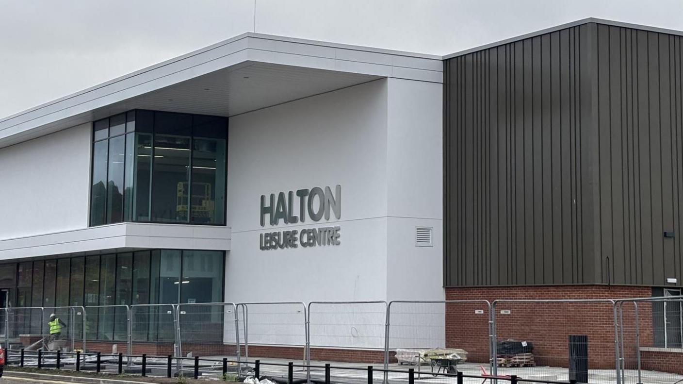 An exterior view of the the new white and brown building with a sign made from silver lettering which reads Halton Leisure Centre 