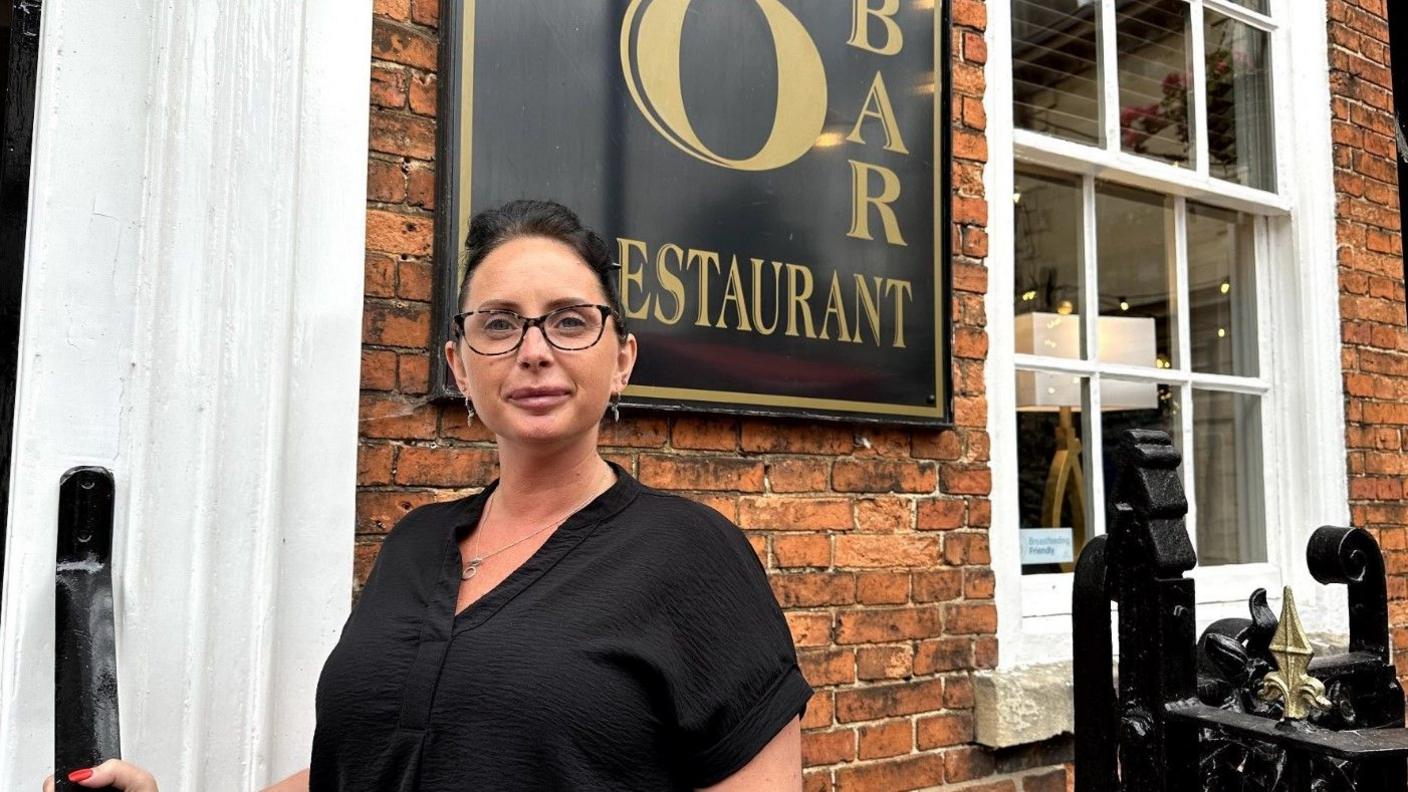 Fran Rawden standing outside her restaurant. She is wearing a black shirt, has her dark hair tied back and is wearing glasses