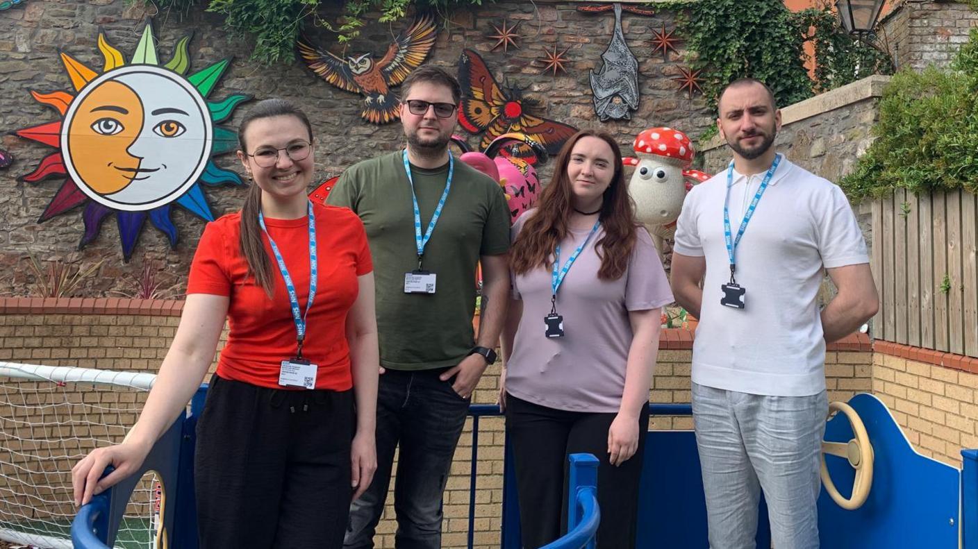 A group of four young Ukrainian medics, two men and two women, stand in a brick-lined play area in a line for the camera outside the Bristol Children's Hospital.