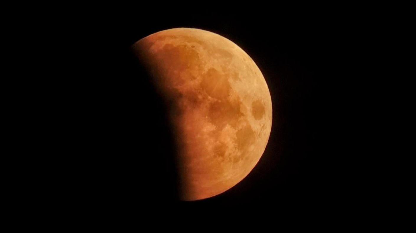 A partial lunar eclipse captured in Charlton Mackrell. The moon is half covered and the other half is orange. The sky behind is black.