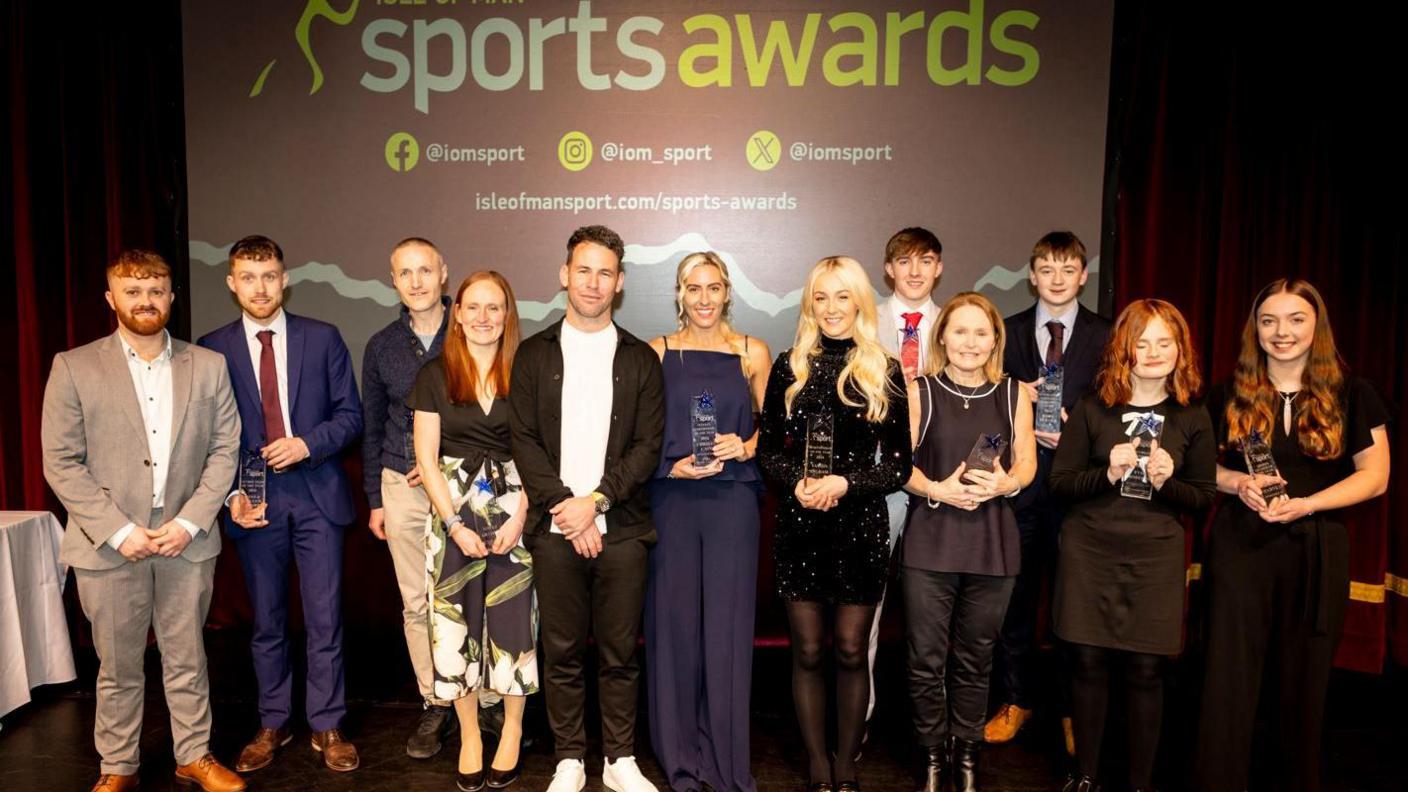 Winners holding their awards lined up in front of a banner that says Sports Awards.