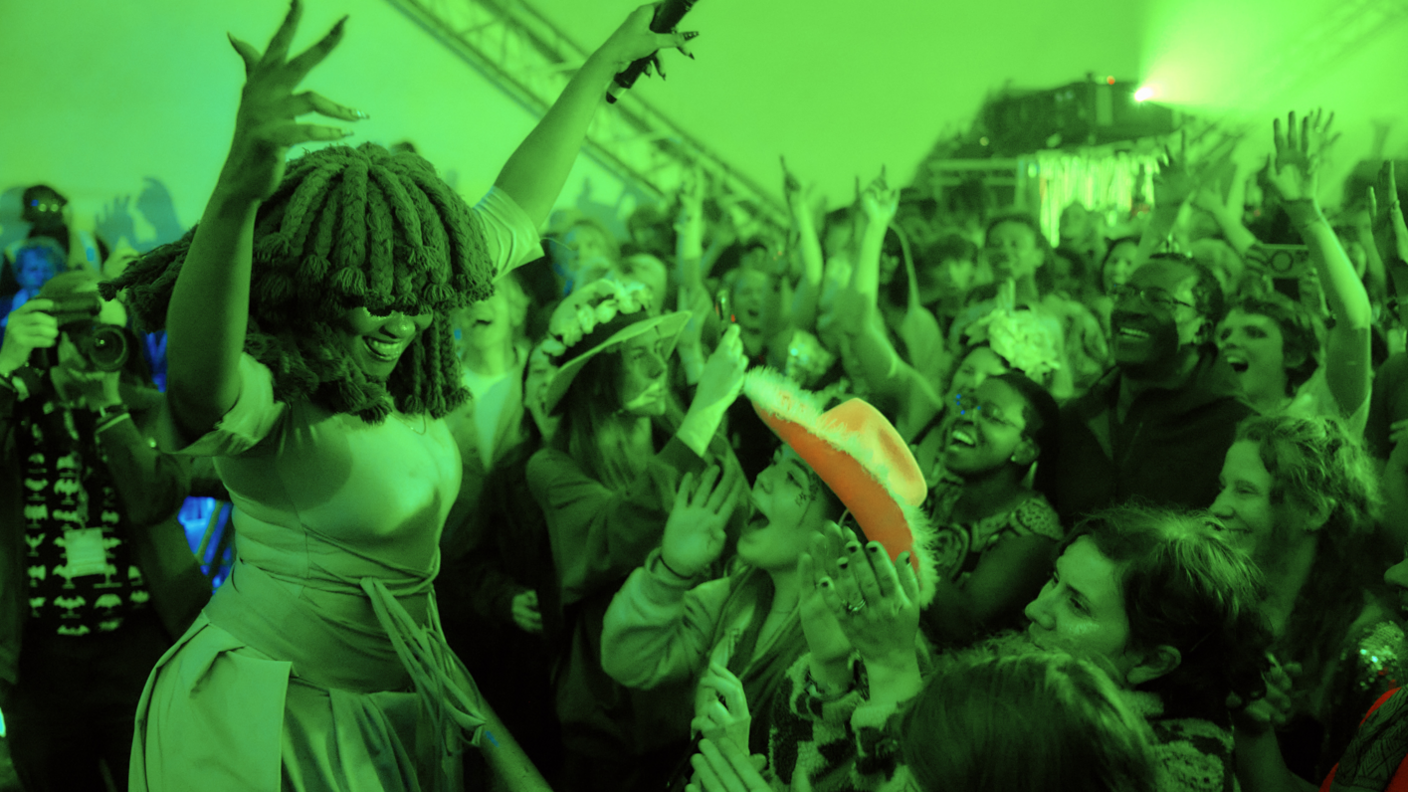 A crowd cheering on a performer on a stage in green lighting