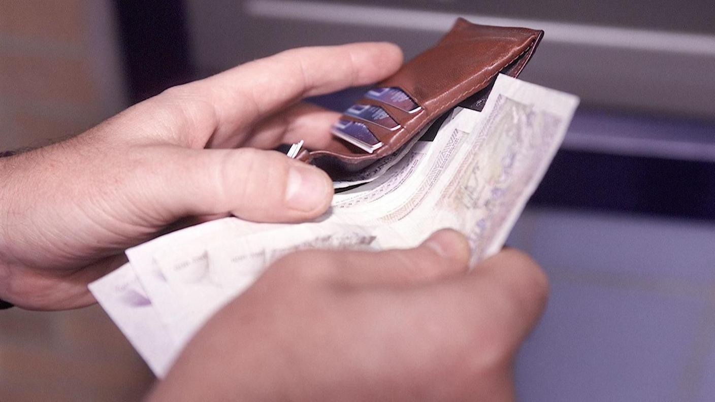 Two are hands are seen taking notes from a brown wallet 