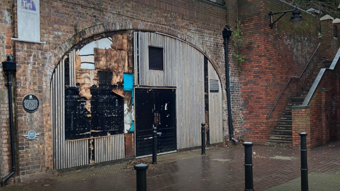 The front of the building in Coventry's canal basin has brick walls, a tin front, and stairs going up from the area outside.