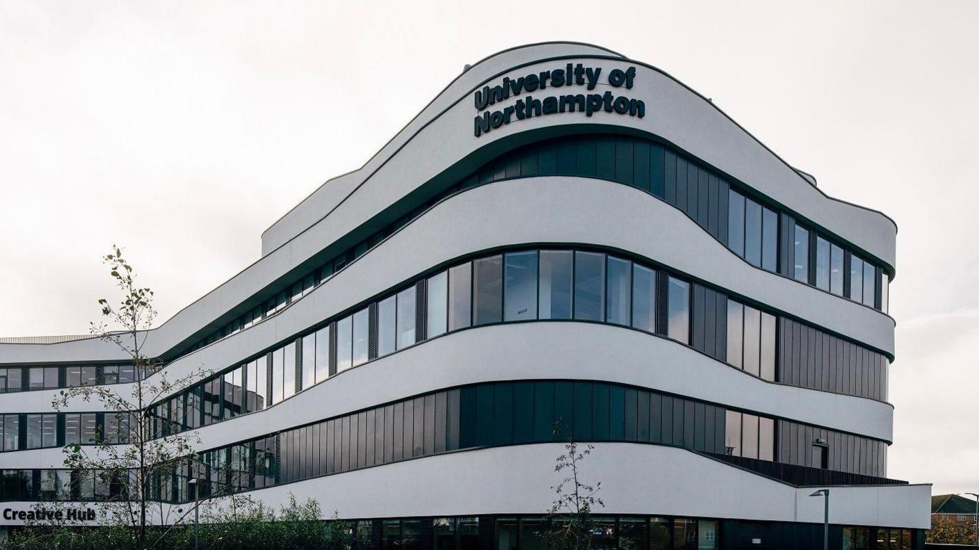 A four-storey modern white curved building with "University of Northampton" sign on the top.