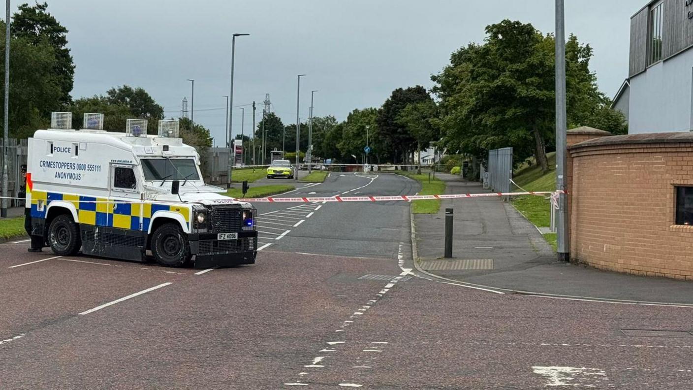 A police vehicle is beside a police cordon.
Another police car is stationed further up a road beside another cordon.