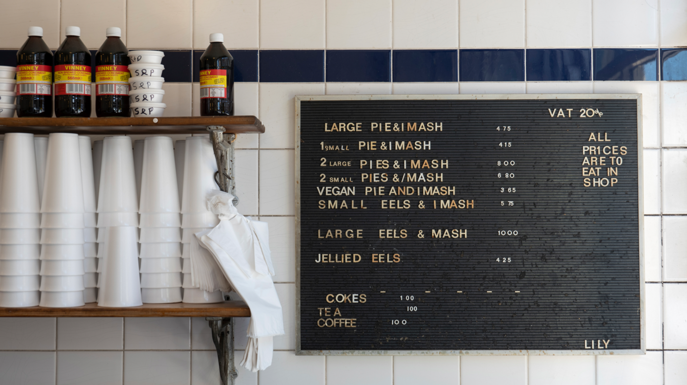 Notice board in pie 'n' mash shop with vinegar and polystyrene cups stacked on the left