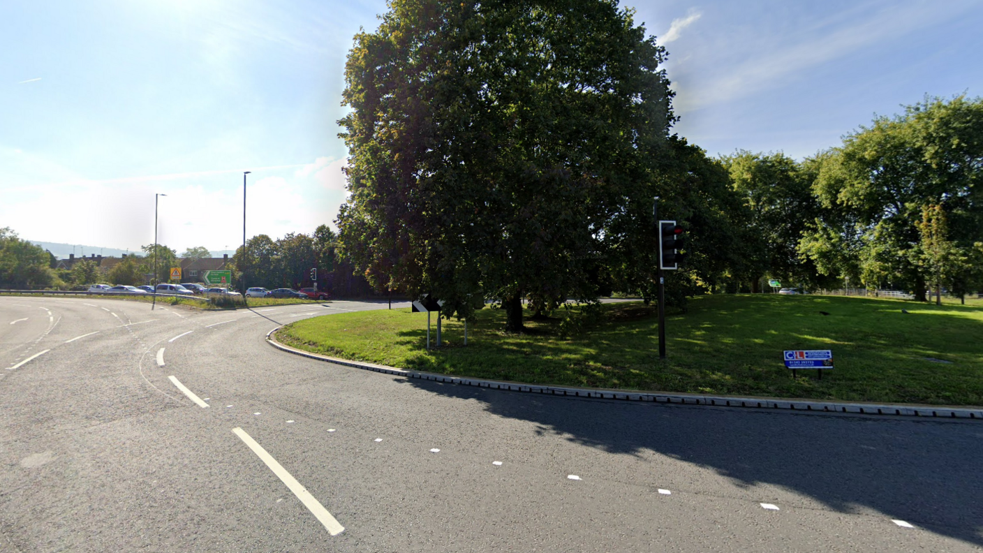 A Google maps image of Benhall roundabout. It is empty with only a few cars in the distance. There are green trees on the roundabout.