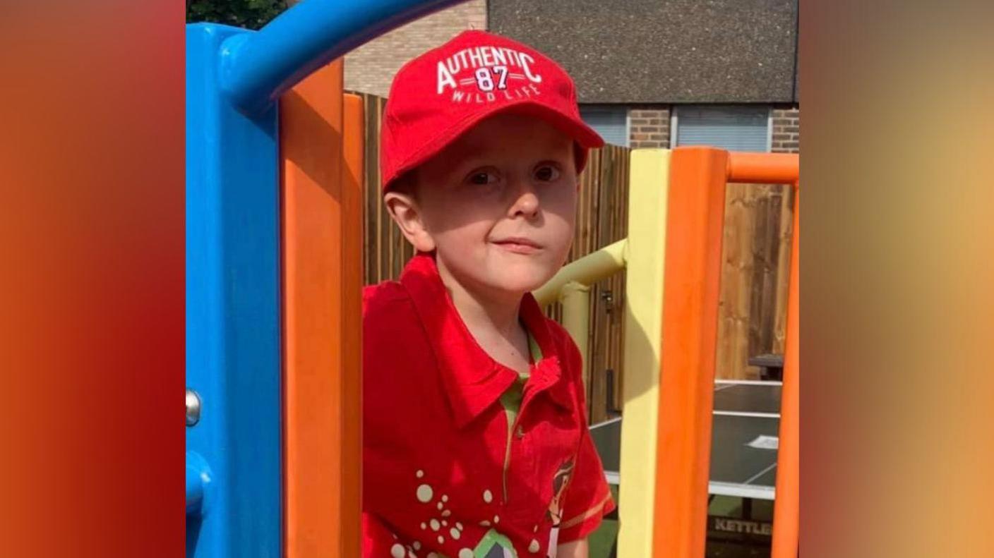 Benny Pitcher stands at the top of a small orange and yellow park slide.