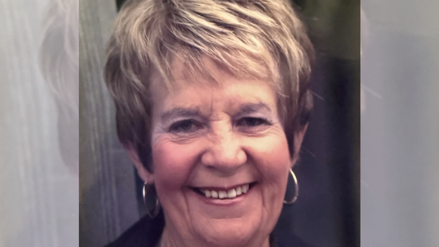 A late middle-aged woman smiling at the camera with partially dyed hair and wearing hooped earrings.