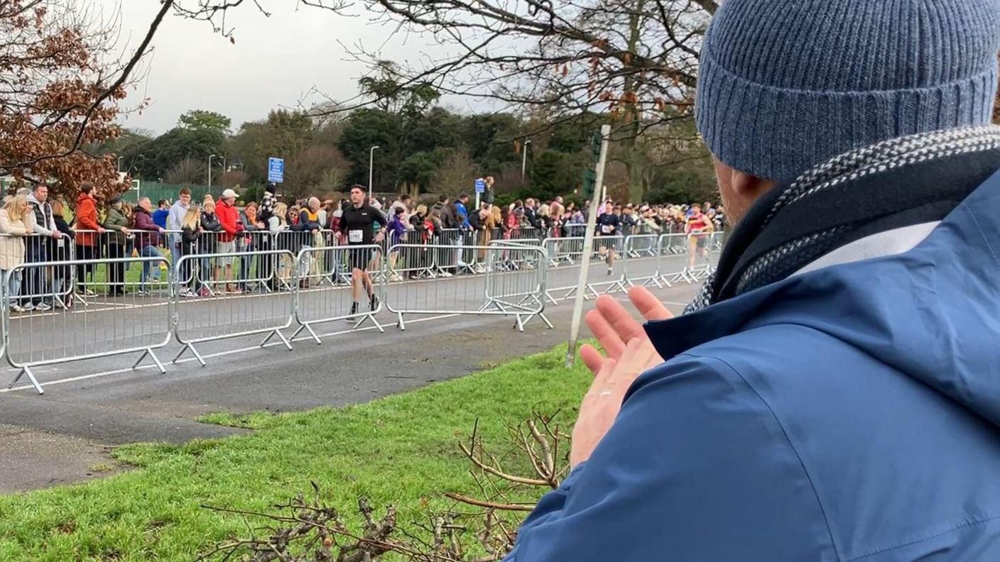 Looking at runners behind a metal barrier while camera looks over someone's shoulder