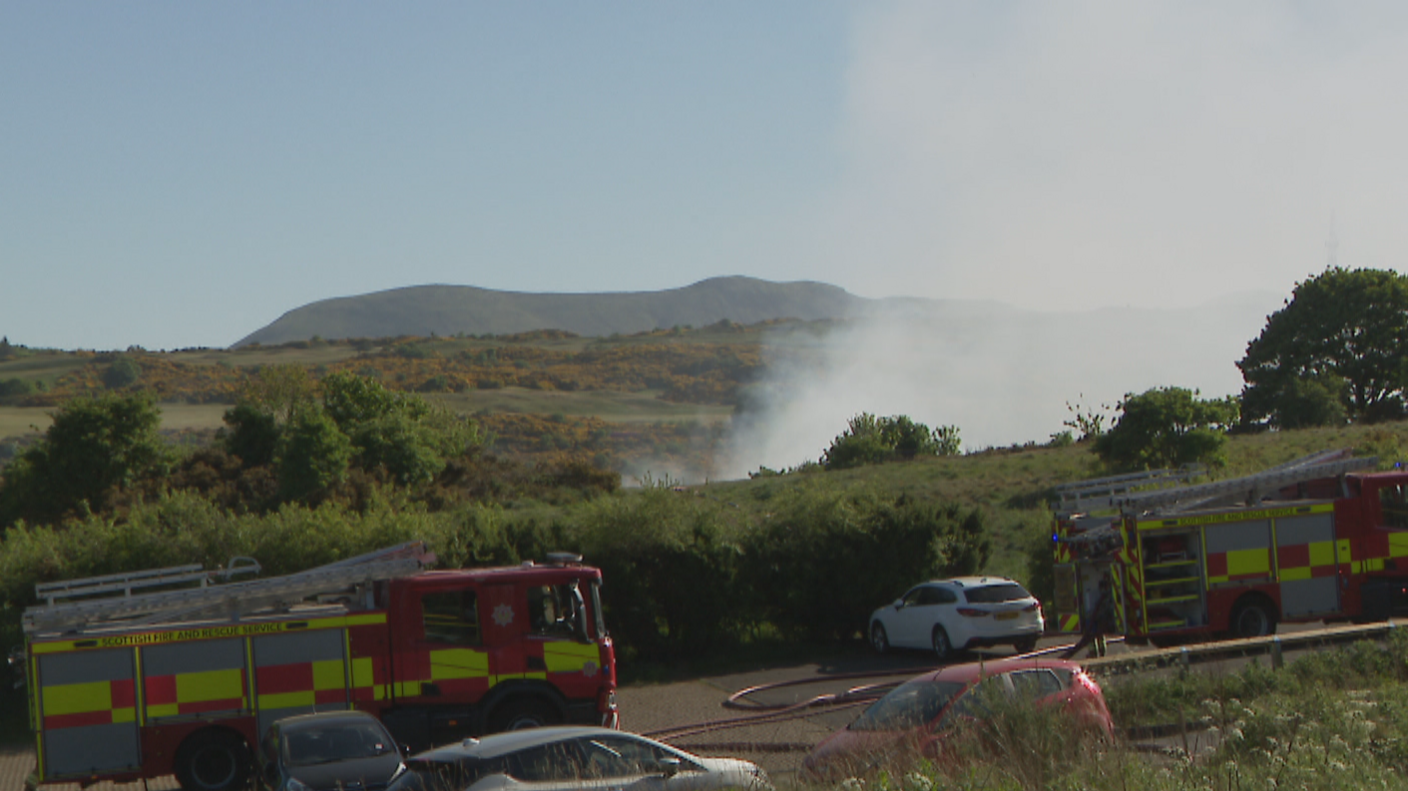 Two fire engines are pictured at the scene of the fire with smoke billowing over the hills