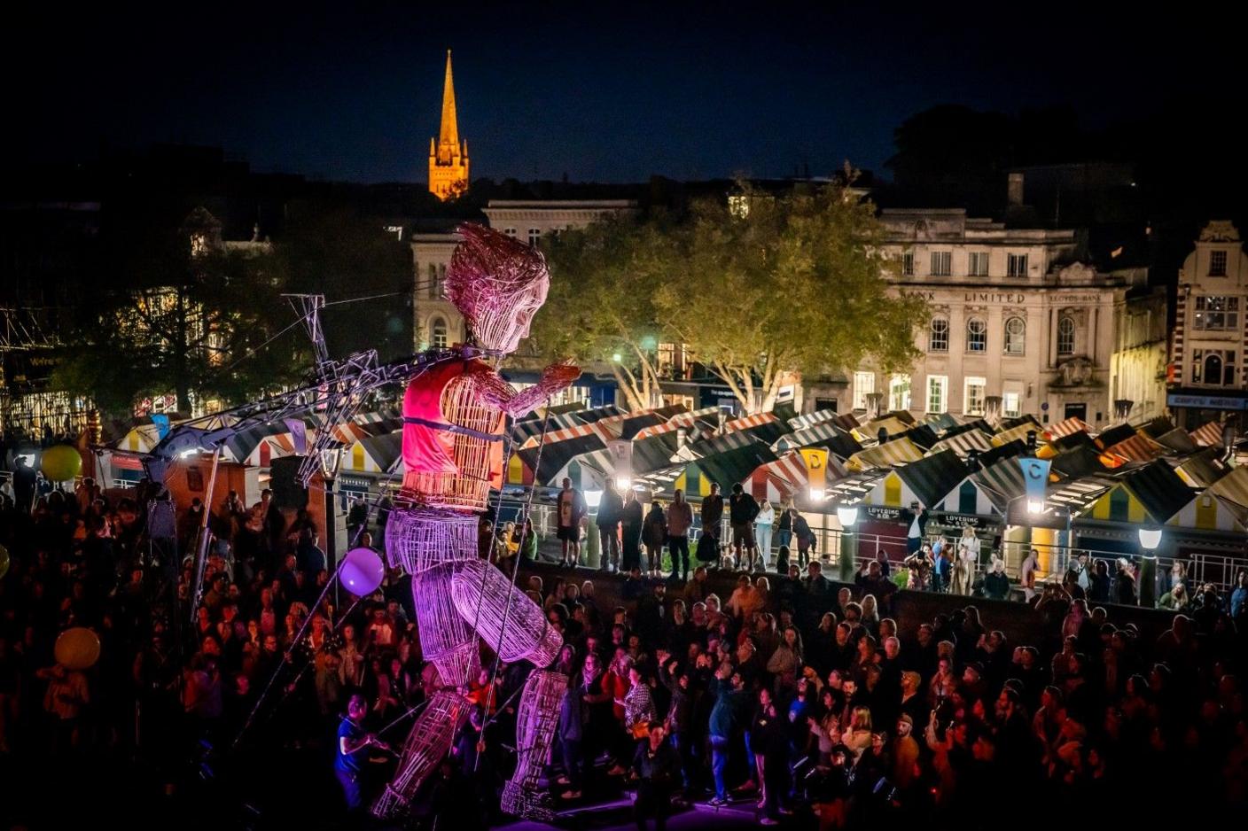 Giant wicker puppet strolls past the top of Norwich Market