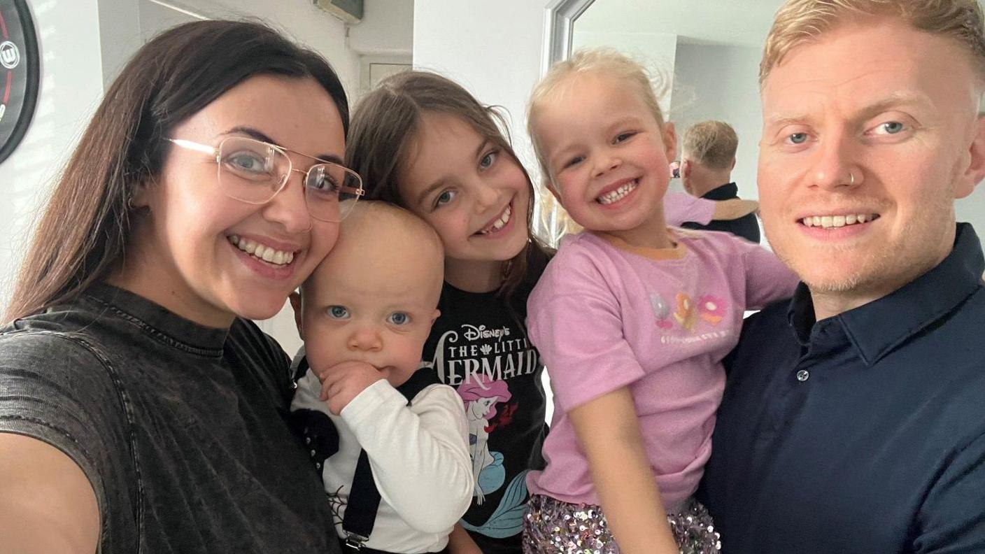 Abigail Hessey smiling for the camera with her three children and partner. Bella is wearing a pink top.