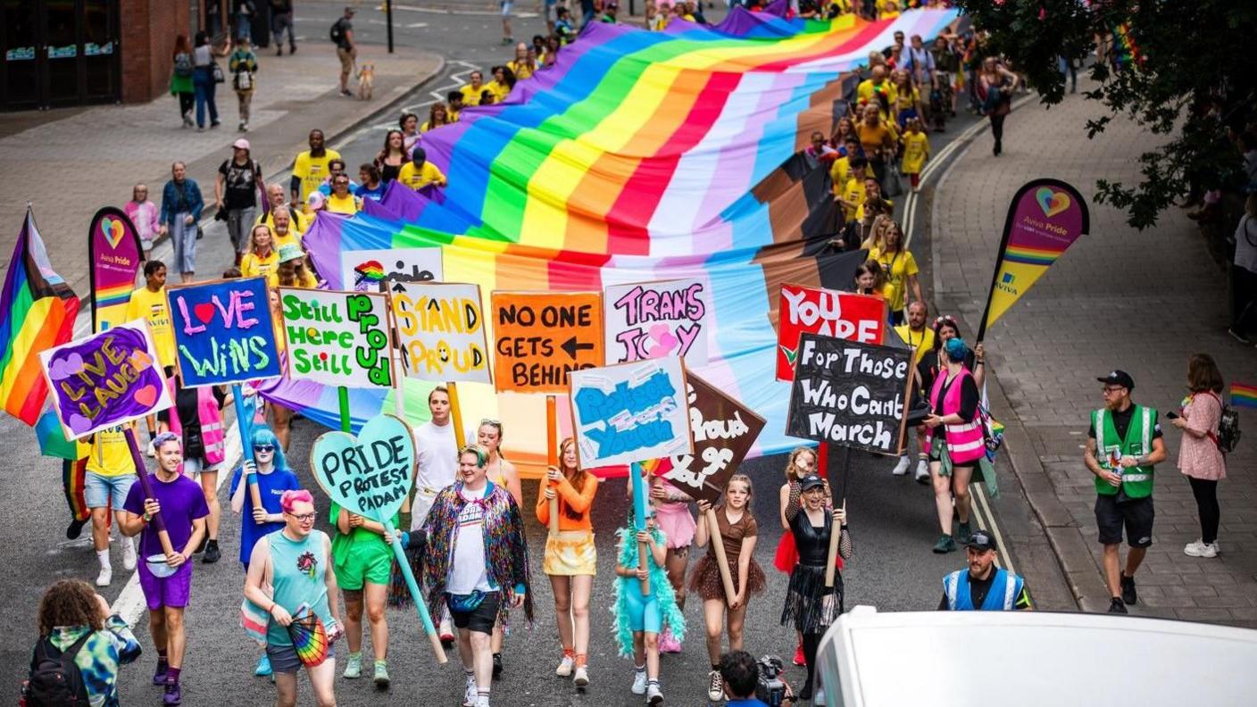 People marching through the street with Pride banners and a rainbow flag