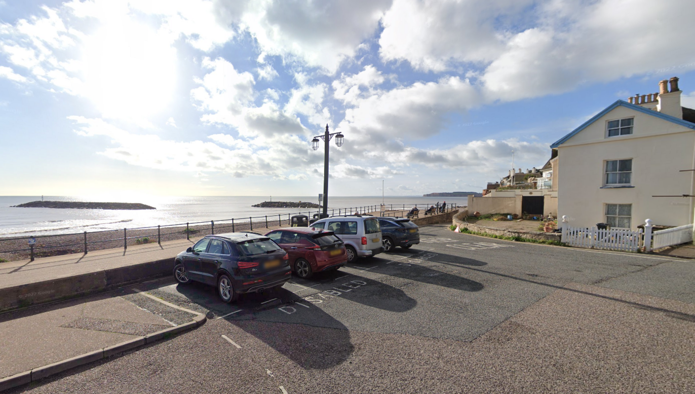 A view from Sidmouth seafront with four cars parked and the sun setting on the beach