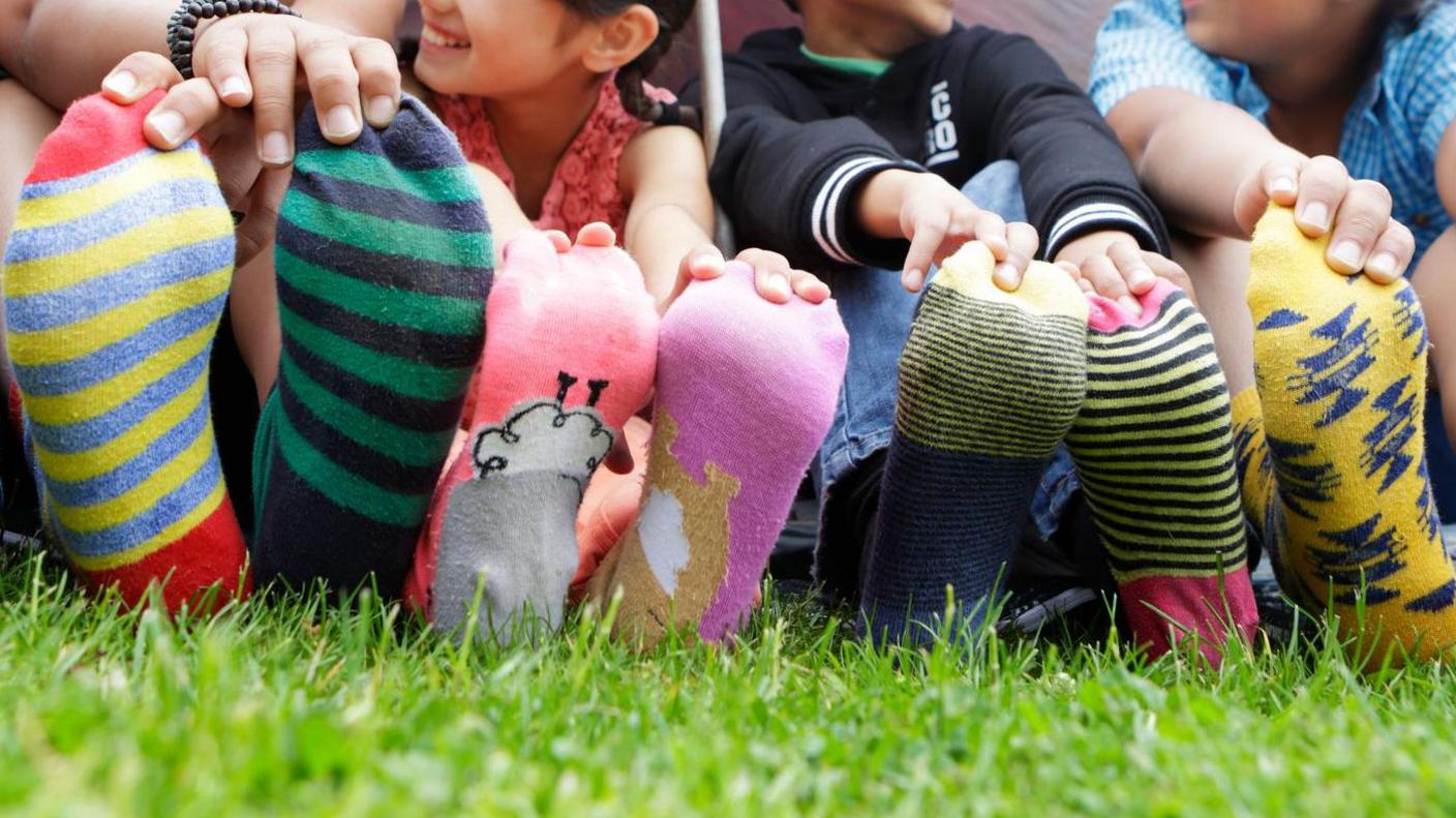 Children wearing colourful patterned odd socks sit on the ground.