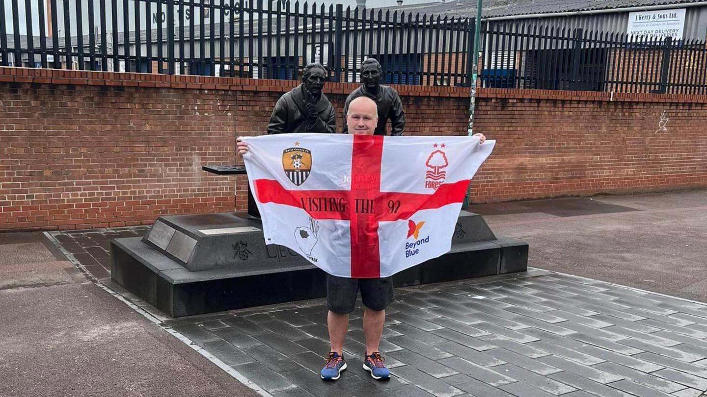 Mr Roome holding an England flag with emblems for mental health charities, Nottingham Forest FC and Notts County FC 