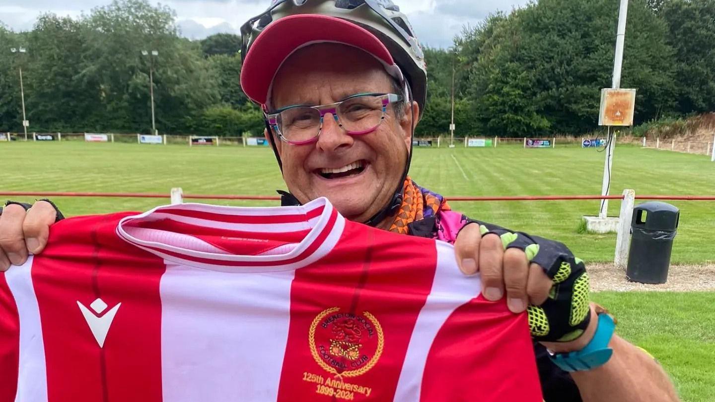 Timmy Mallet wearing cycling gear and holding a red and white football shirt