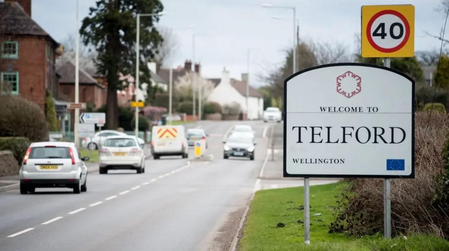 A large white welcome to Telford sign alongside a road with a number of cars on it