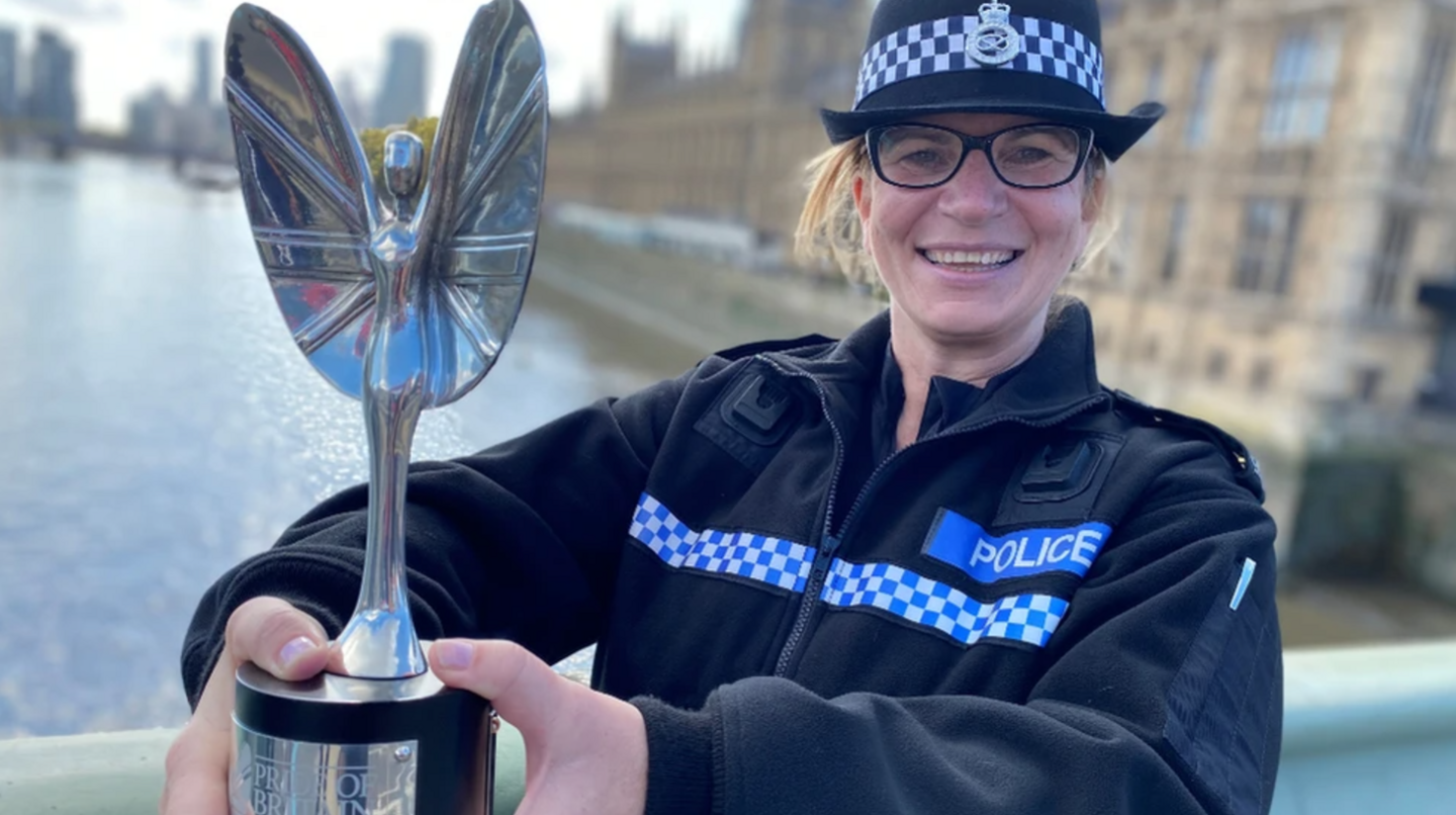 A police officer in her uniform, holding a silver trophy with a silver winged figure on top