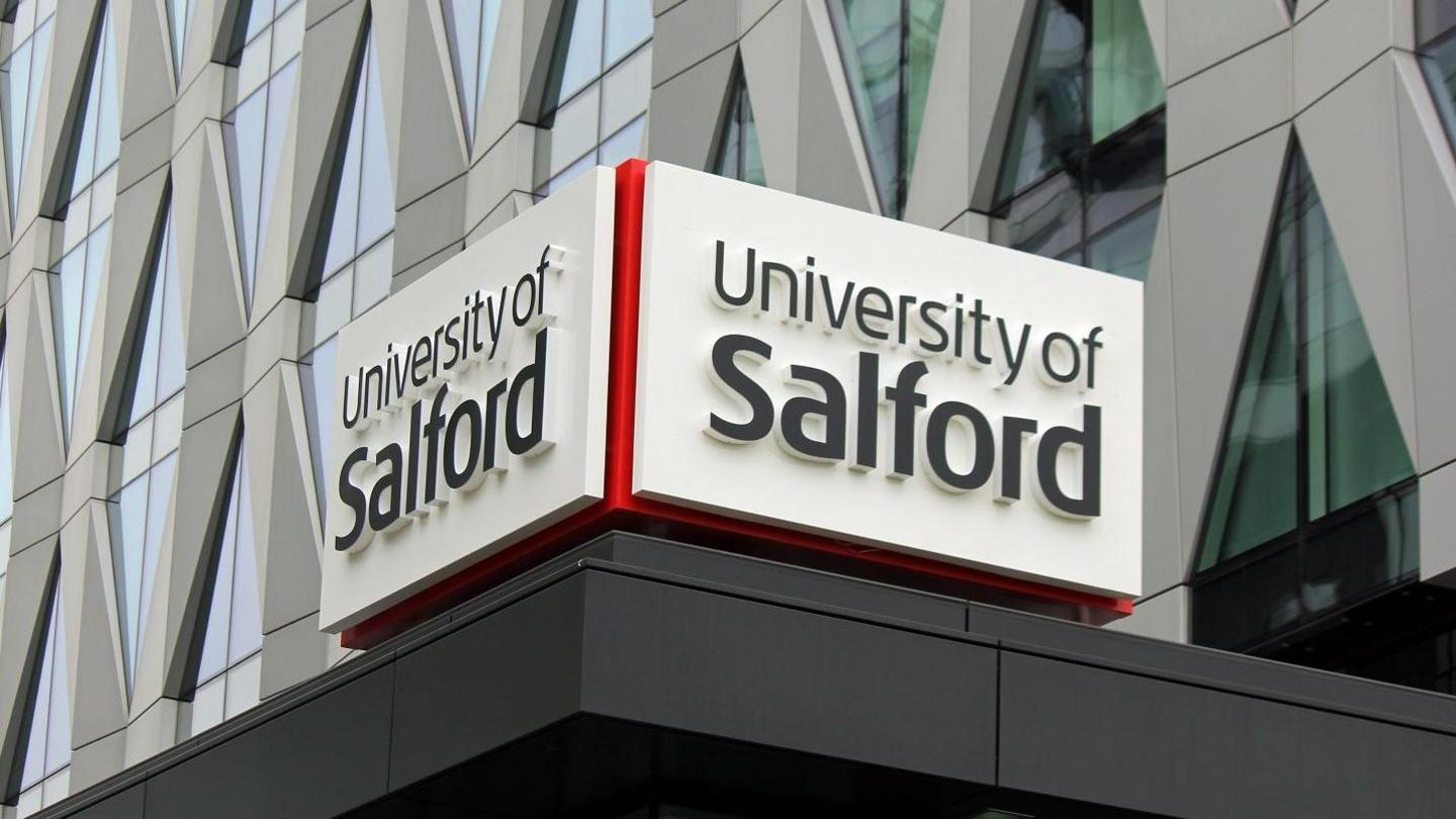 University of Salford logo above a building entrance backed up by a modern criss-cross building design