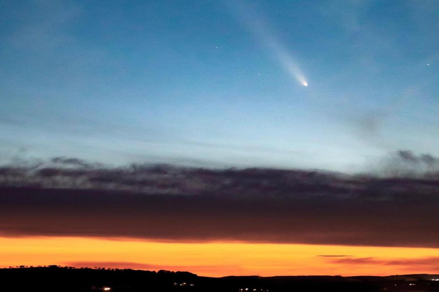 Comet A3 appears above clouds. There is the golden glow of sunset.