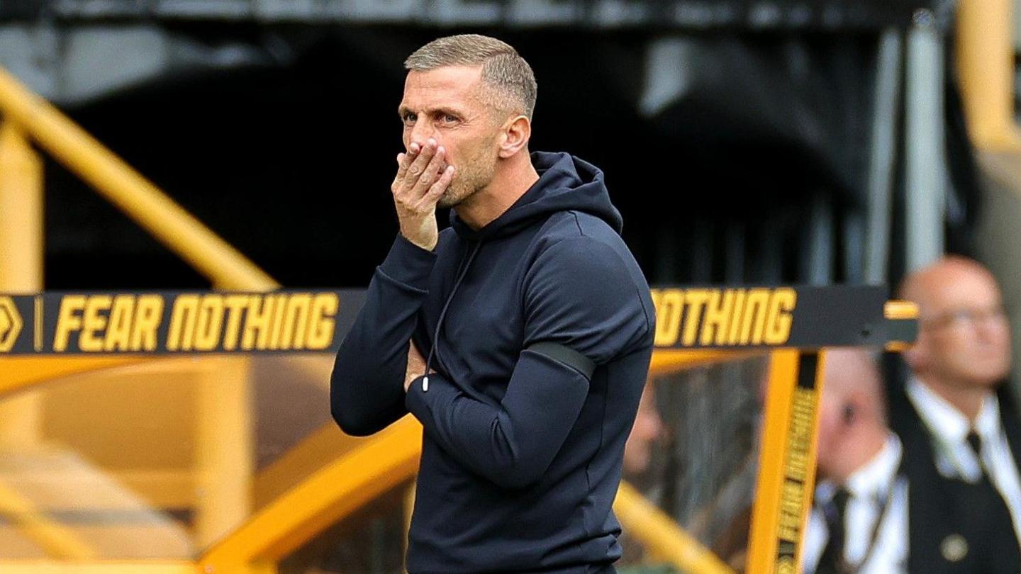 Gary O'Neil holds his right hand to his mouth while he stands in front of the Wolves' dugout. 