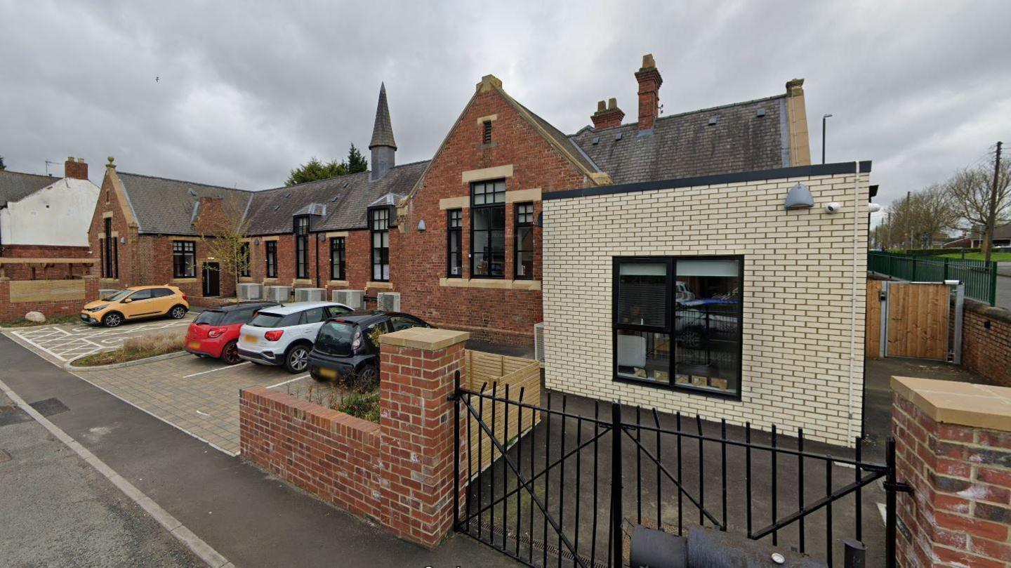 An external view of Old School House. The apartments are based inside an old school building and cars are parked in the car park.