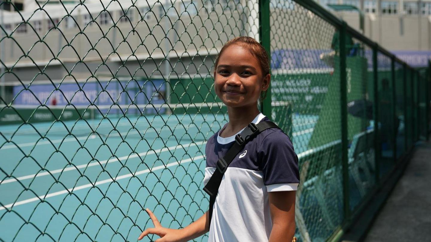 Maristella Torrecampo, a Filipina tennis player and fan of Alex Eala, standing on the side of a tennis court in Manila