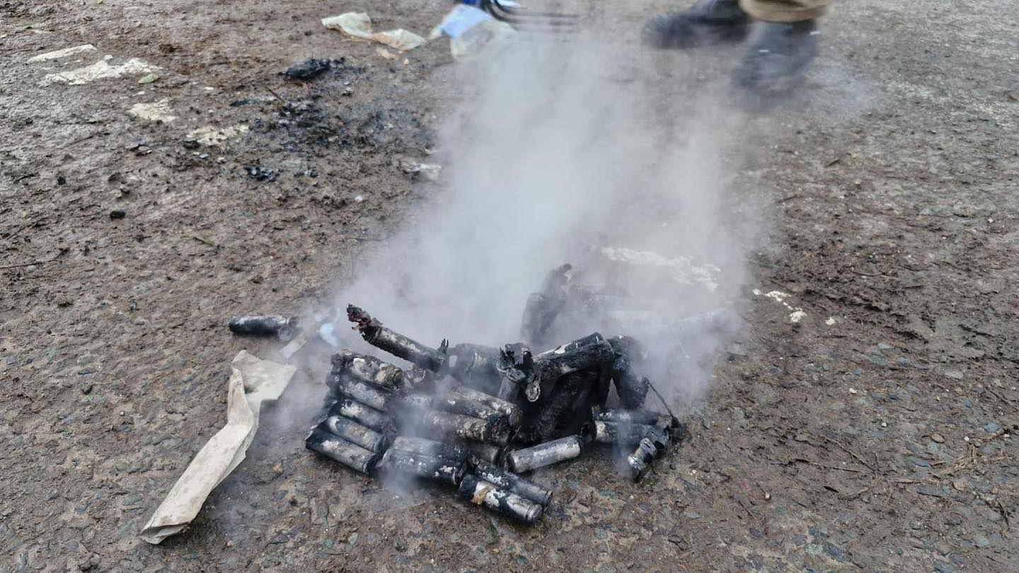 A blackened pile of burned out batteries lies on a road, with smoke still emanating. 