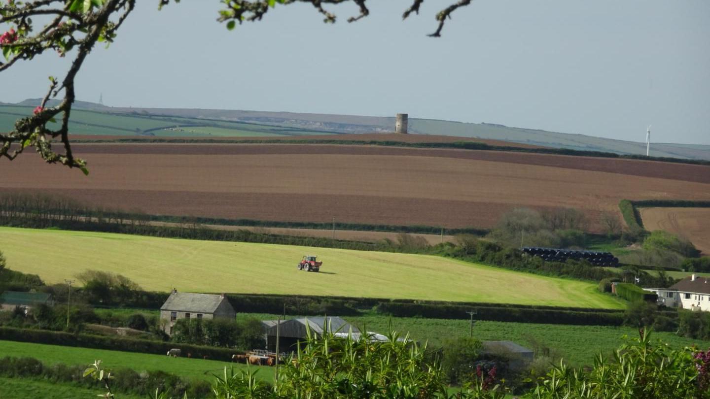A red tractor goes around a field in the St Minver area of Cornwall. It is an overcast day.