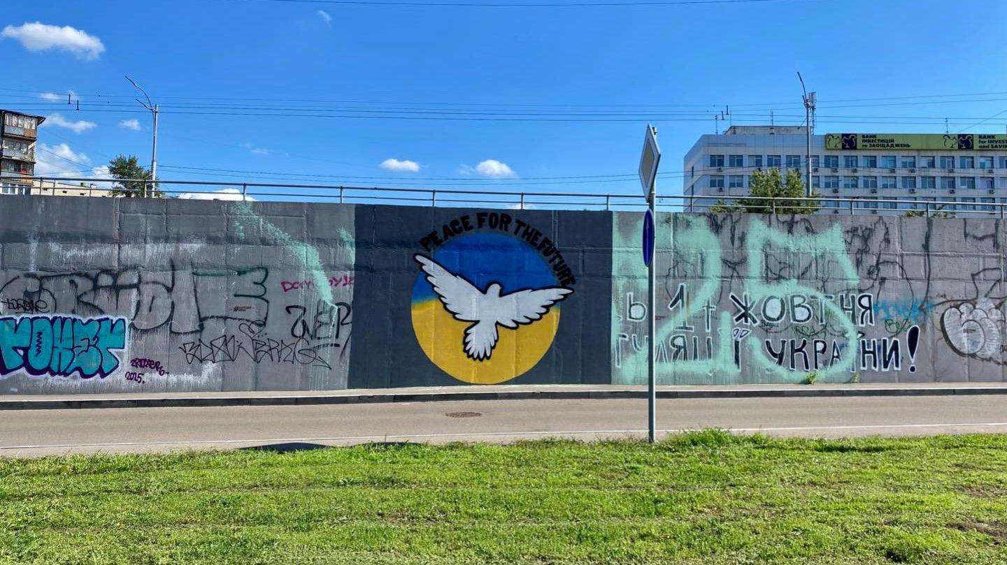 A Ukrainian flag mural on the side of a highway with a peace dove flying out from it, with the words "peace for the future" in English.