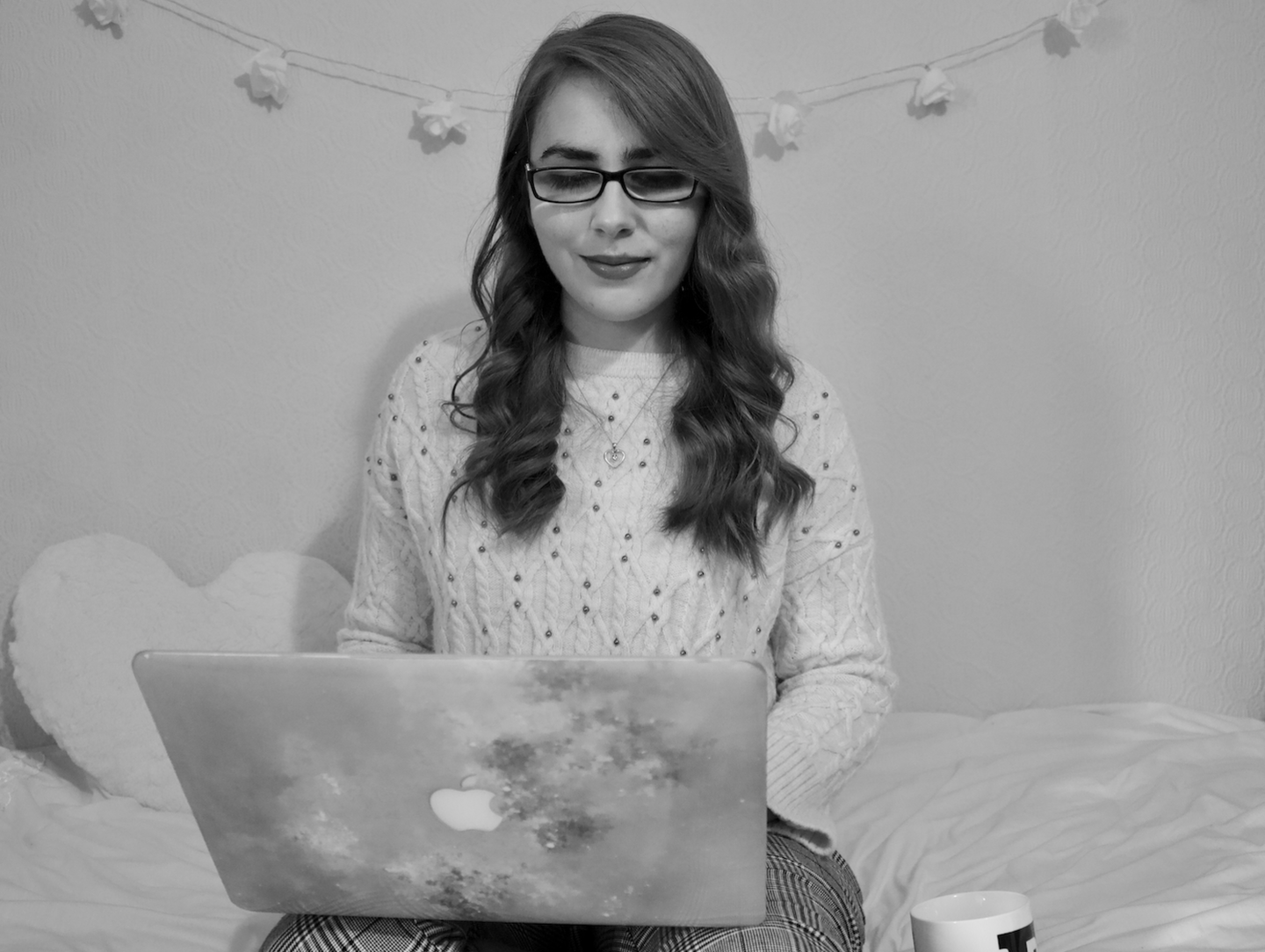 Elin sitting on a bed with a love heart cushion behind her, working on a laptop