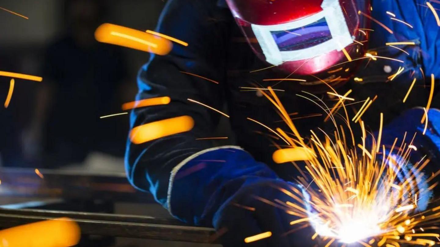 A person in protective gear welding a piece of metal. Sparks are flying.