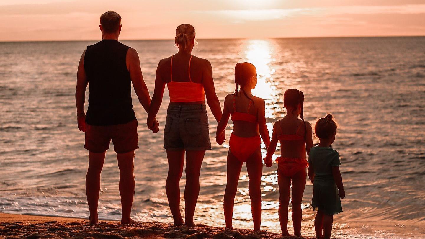 The family face the sunset on a beach