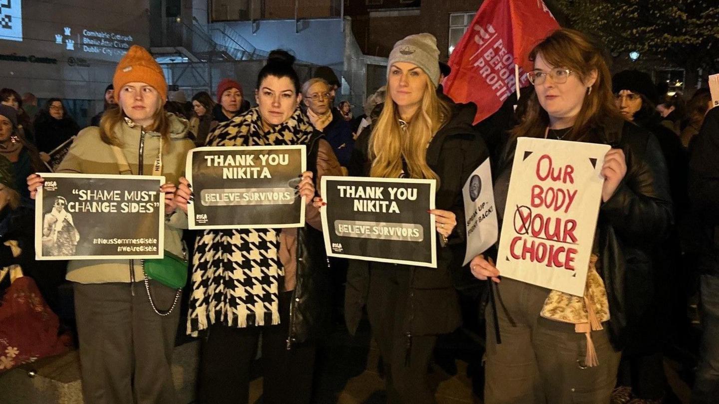 A group of women stand on a winter's evening in Dublin, as part of a rally in support of Nikita hand who won a civil case against Irish mixed martial arts (MMA) fighter Conor McGregor. They are wearing signs saying 'thank you nikita'.