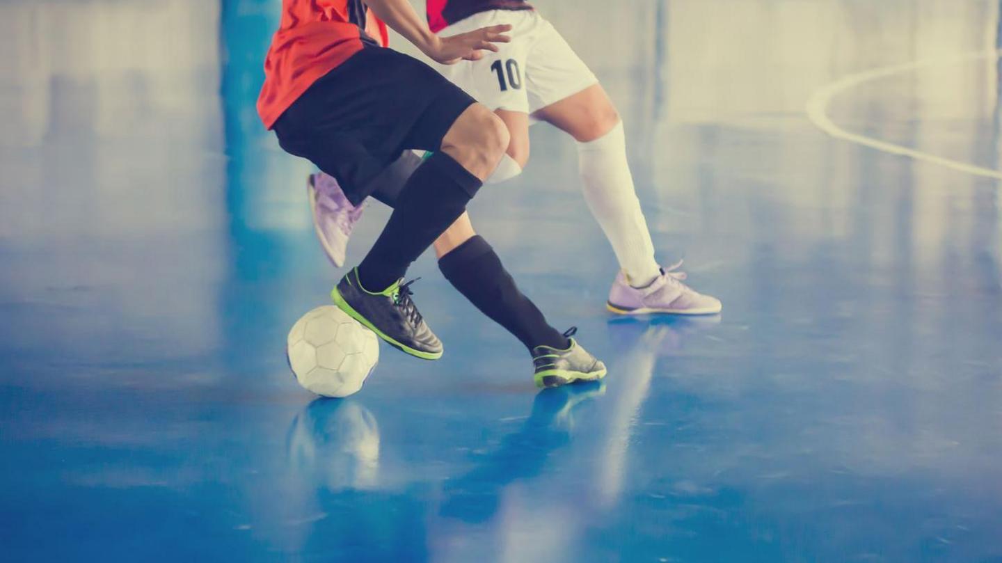 Two people playing futsal - image shows them from the waist down on a blue court 