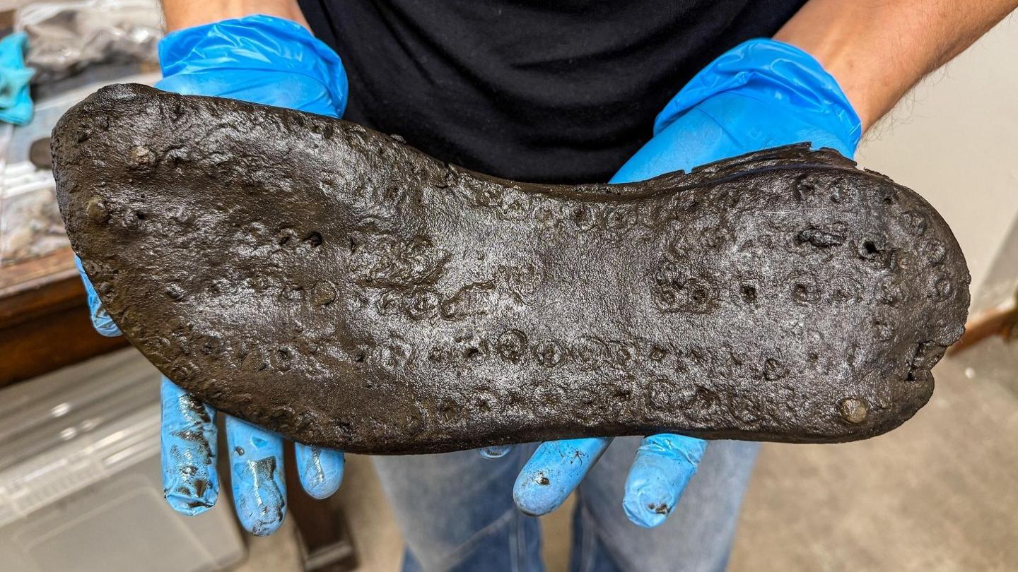 The bottom of a large shoe, being held by a woman wearing blue plastic gloves