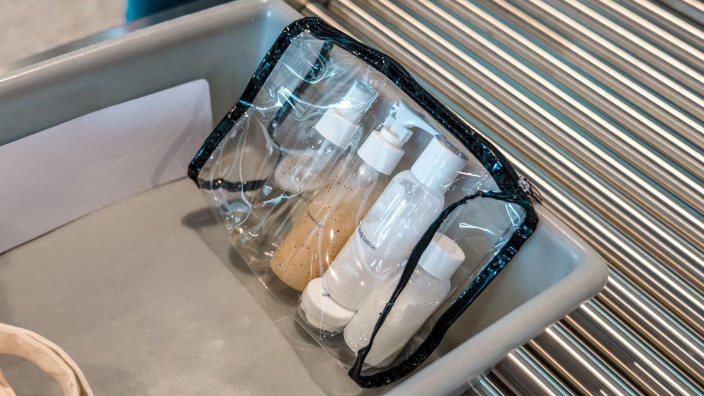 Four small bottles of liquid in a clear plastic zip-up case. It is on a plastic tray on an airport security conveyor belt