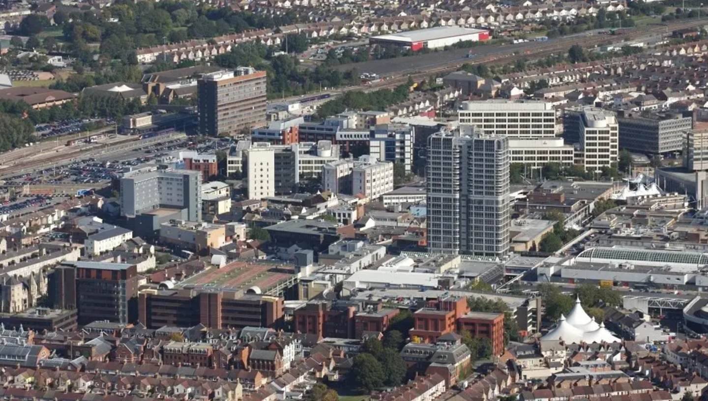 Skyline view of Swindon showing various tall buildings, offices and homes with a train station in the distance.