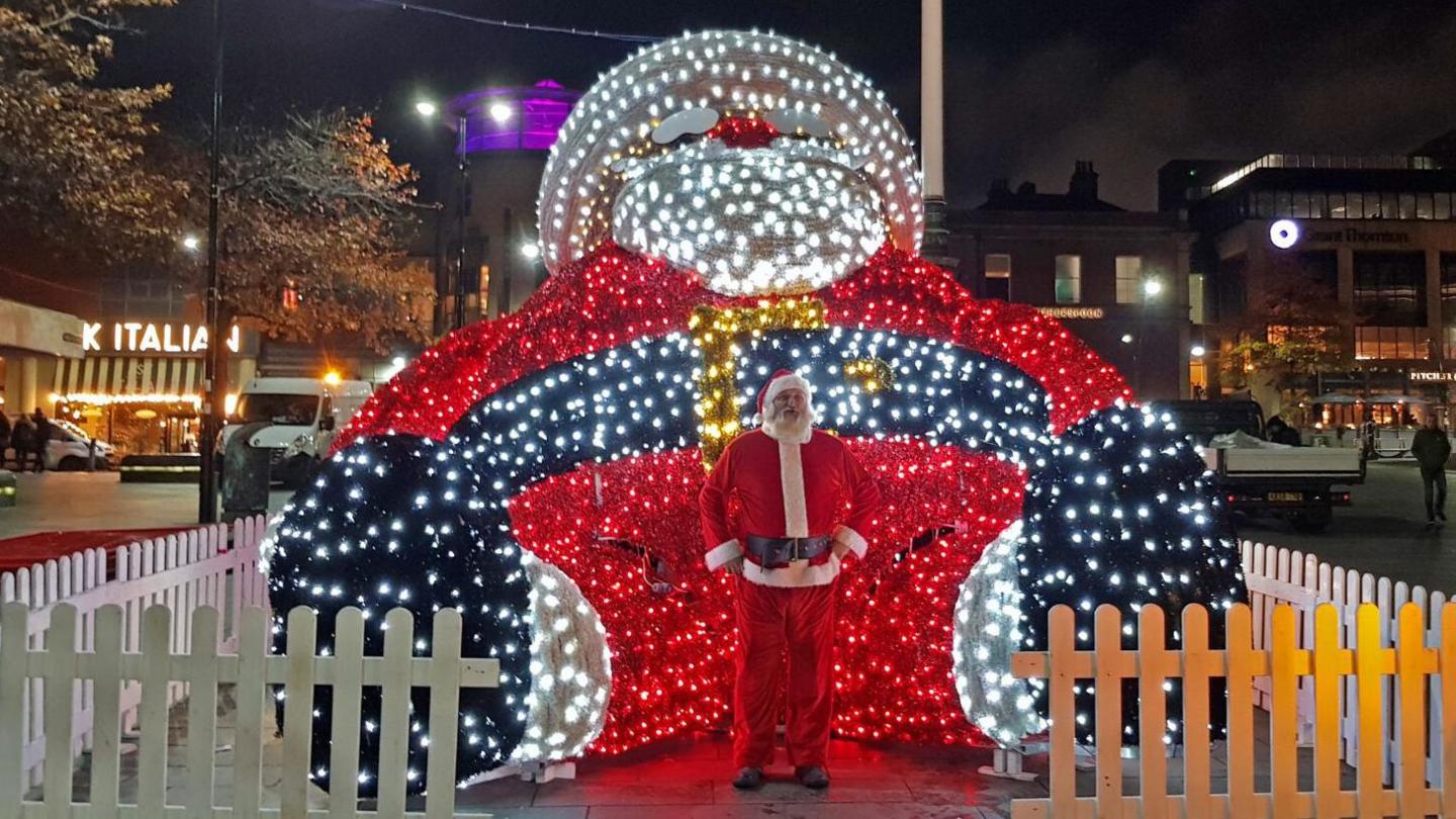 The UK's largest light-up Santa installation behind a man who is dressed up as Santa Claus himself