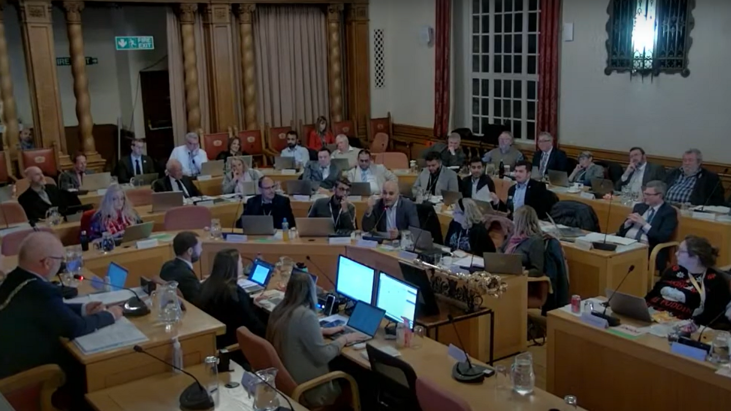 Council meeting in progress- with councillors sitting on wooden tables in a semi-circle with the mayor sitting in front alongside council officers.