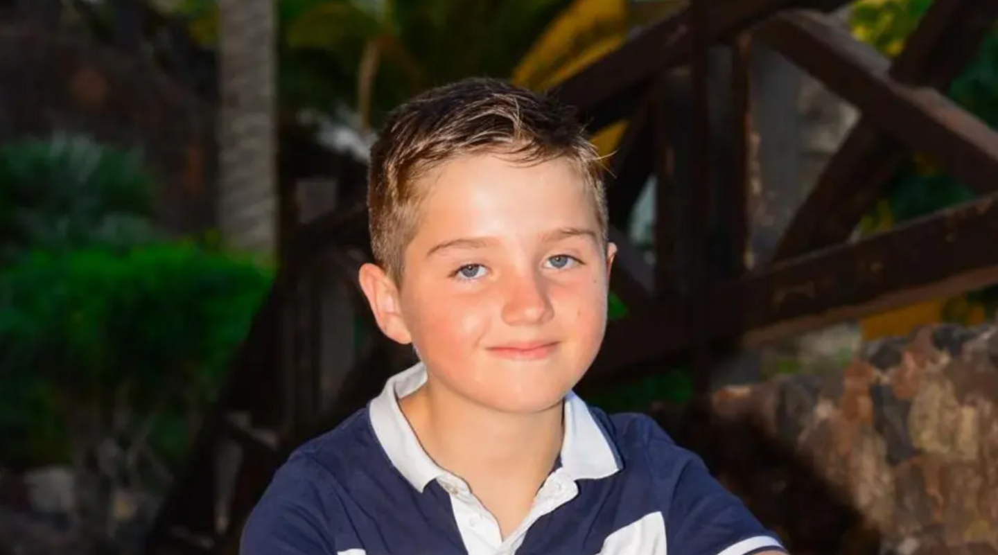 A young boy with brown hair wearing a blue and white polo smiling into the camera