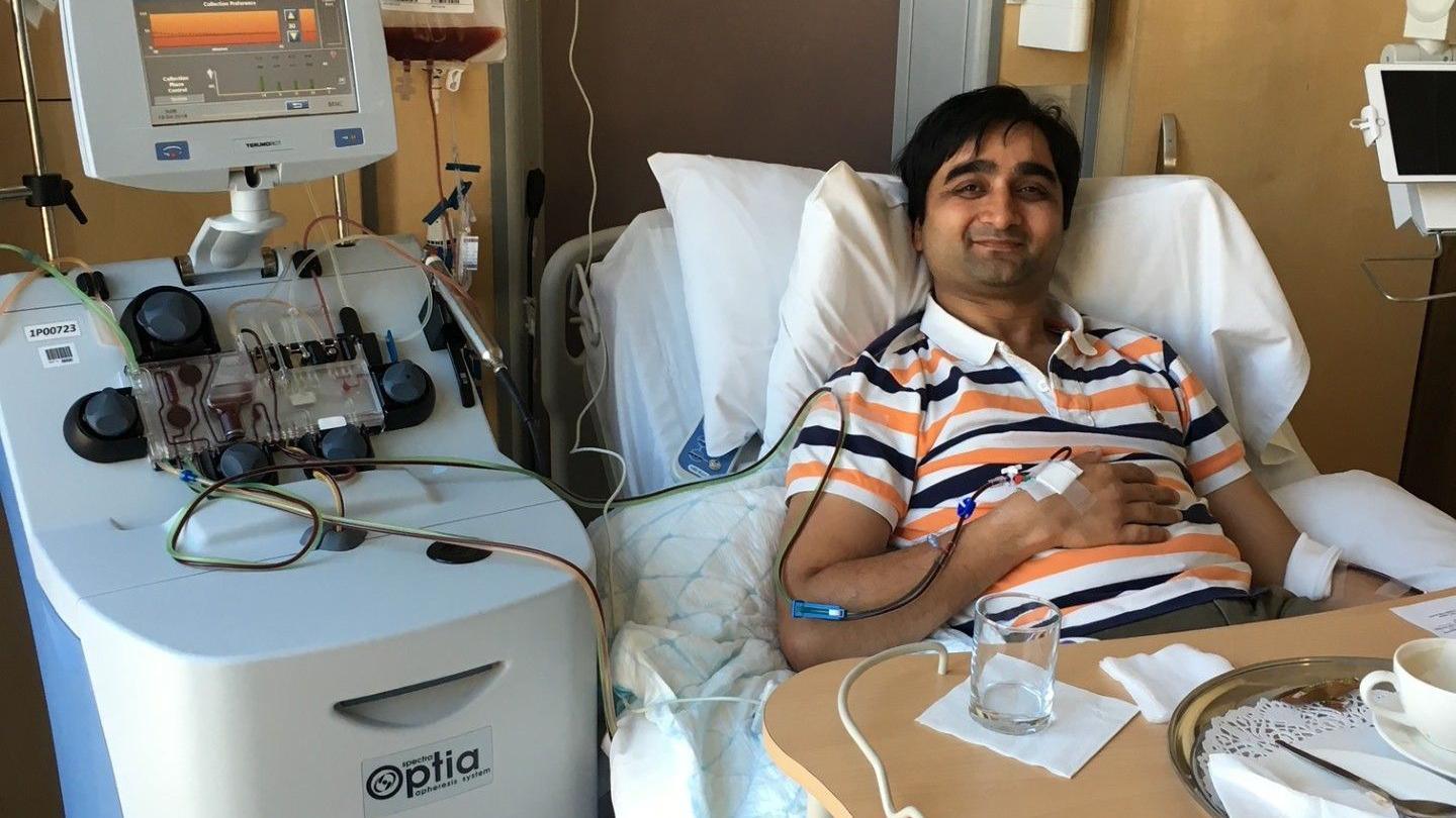 Nirav donating stem cells wearing a stripy shirt in a hospital bed smiling