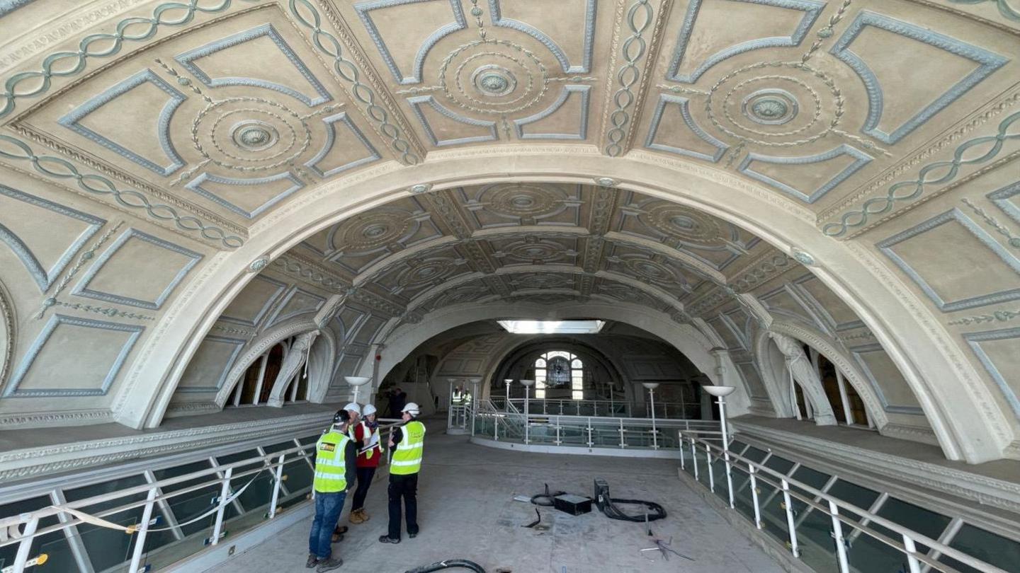 In the foreground Torbay Council's team of architects and engineers discuss the work that needs to be done. Above them is a decorative white and blue plaster ceiling.