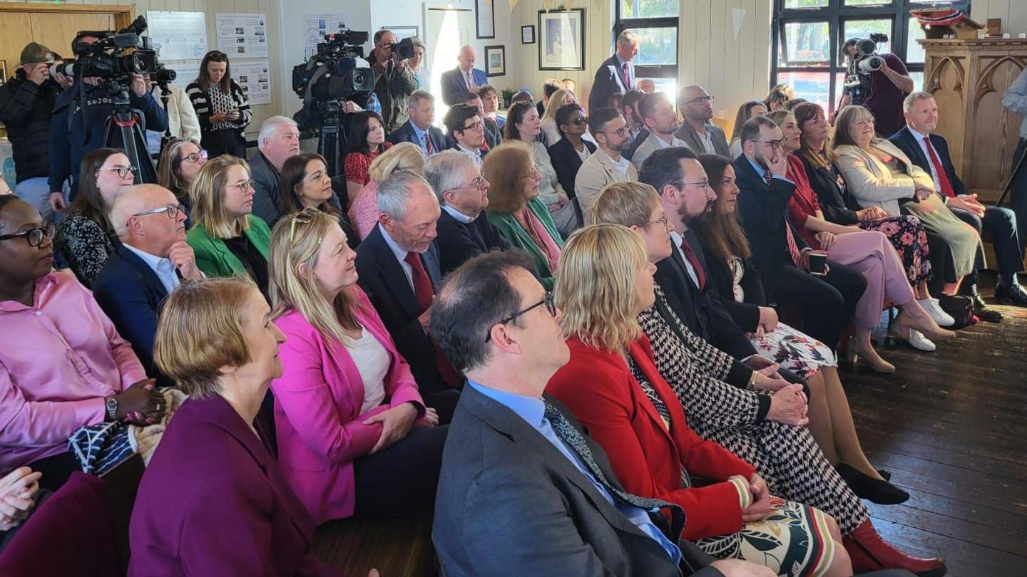 A group of Labour politicians and party members sat listening to Eluned Morgan, with Jayne Bryant, Lee Waters, Jeremy Miles and Mark Drakeford among them.