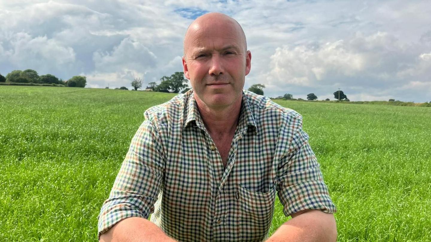 Farmer Charlie Goadby is dressed in a check shirt and is in sun-lit field for crops 