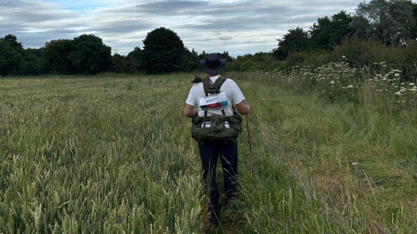 Philip with his back to the camera walking through a field of grass with a walking stick