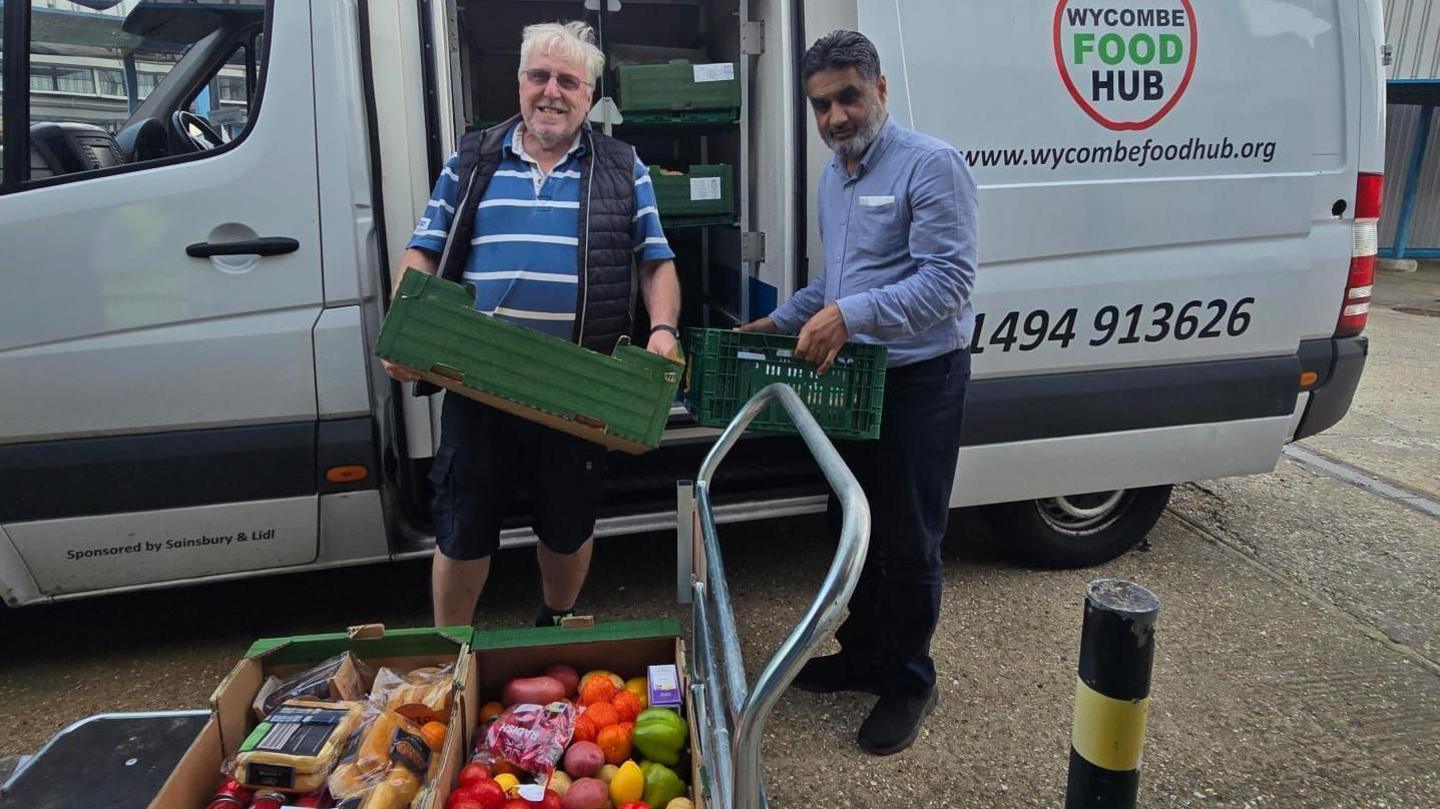 Two men are unloading green food baskets from a van.
